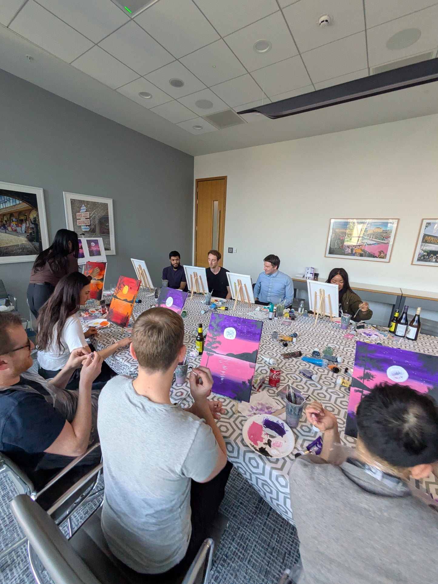 Group of people sitting around an office table with art supplies, engaged in a painting activity as a team building event with Judy Century Art.