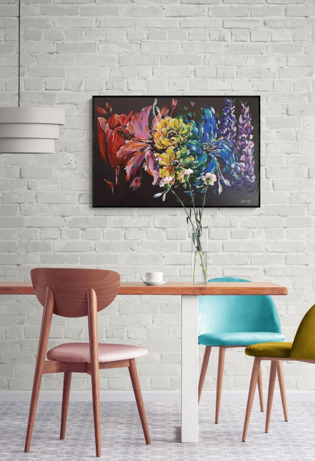 Multi-coloured abstract Carnival Rainbow flower painting on contrasting black background by Judy Century Art. home decor inspiration wall art shown on white brick wall above wooden dining table with colourful blue, mustard yellow and blush pink chairs