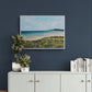 Expressive landscape painting of a calm beach viewed from a grassy headland. Hanging above a light gray cabinet with gold handles against a dark blue wall. Artwork by Judy Century Art.