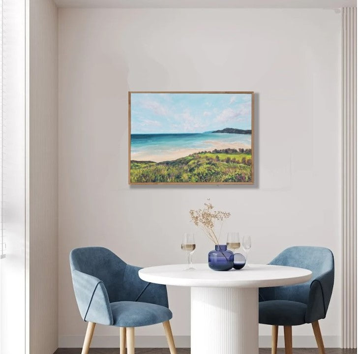 Dining room with a round table and two blue chairs, featuring a framed landscape painting on the wall.