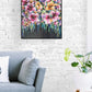 Colourful Floral Canvas painting of abstract flower bouquet by Judy Century. Shown framed in black above grey couch with white cushion against a white brick wall.