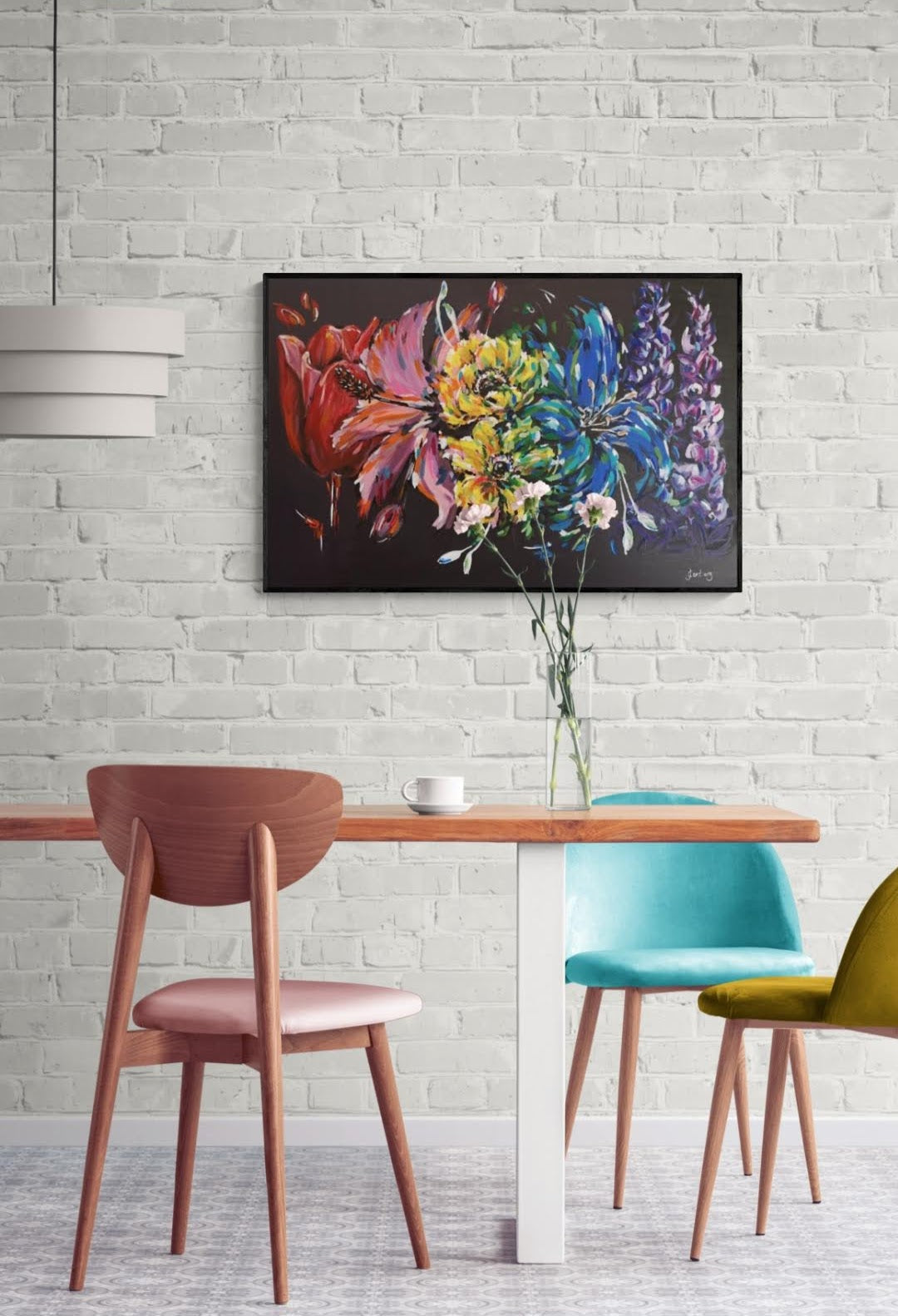 Multi-coloured abstract Carnival Rainbow flower painting on contrasting black background by Judy Century Art.  home decor inspiration wall art shown on white brick wall above wooden dining table with colourful blue, mustard yellow and blush pink chairs