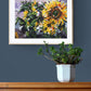 Expressive Sunflower acrylic painting on paper by Judy Century. Yellow, Green and purple wall art. shown on a navy wall above wooden sideboard.