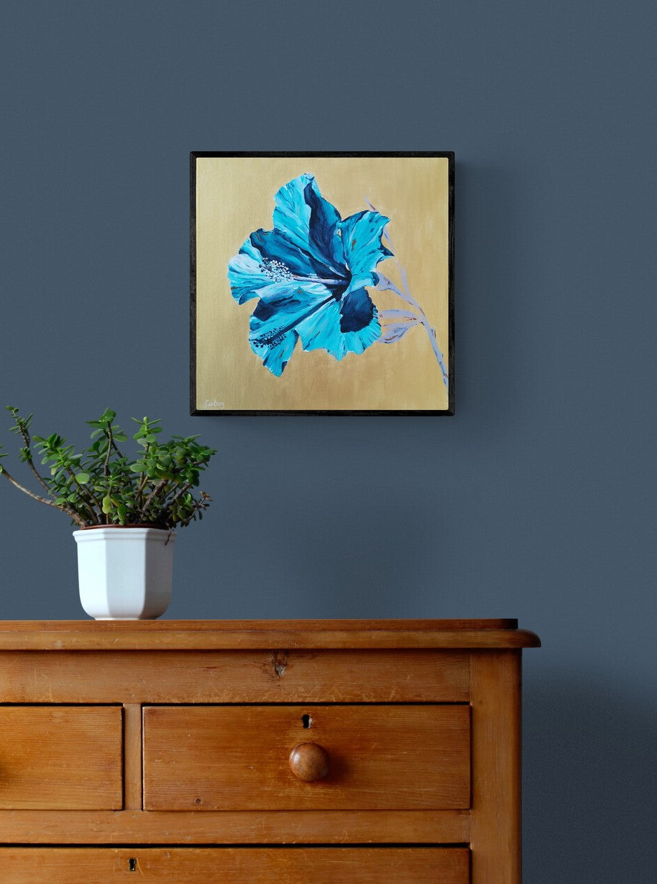 Modern floral canvas painting of turquiose hibiscus flower by Judy century art shown on navy blue wall with plant accessory and wooden chest