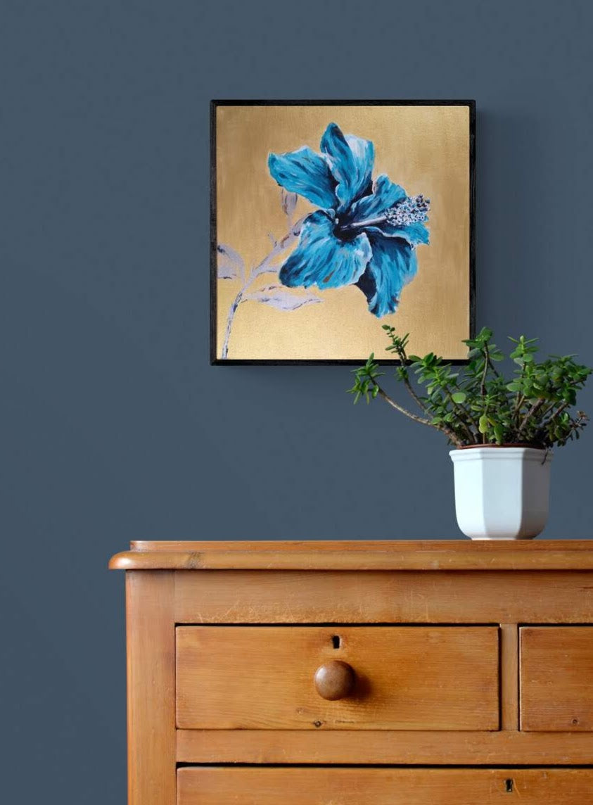 Contemporary original gold and turquoise blue painting of hibiscus flower by Judy Century Art shown in modern navy interior with wooden chest of drawers