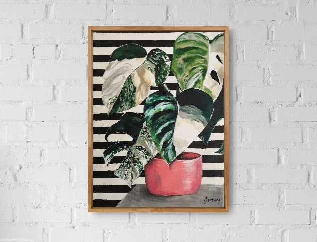 Plant painting, variegated Monstera cheese plant acrylic painting on A4 canvas with bold black and white striped pattern background. Painting hangs on white brick wall with an oak frame for wall art ideas